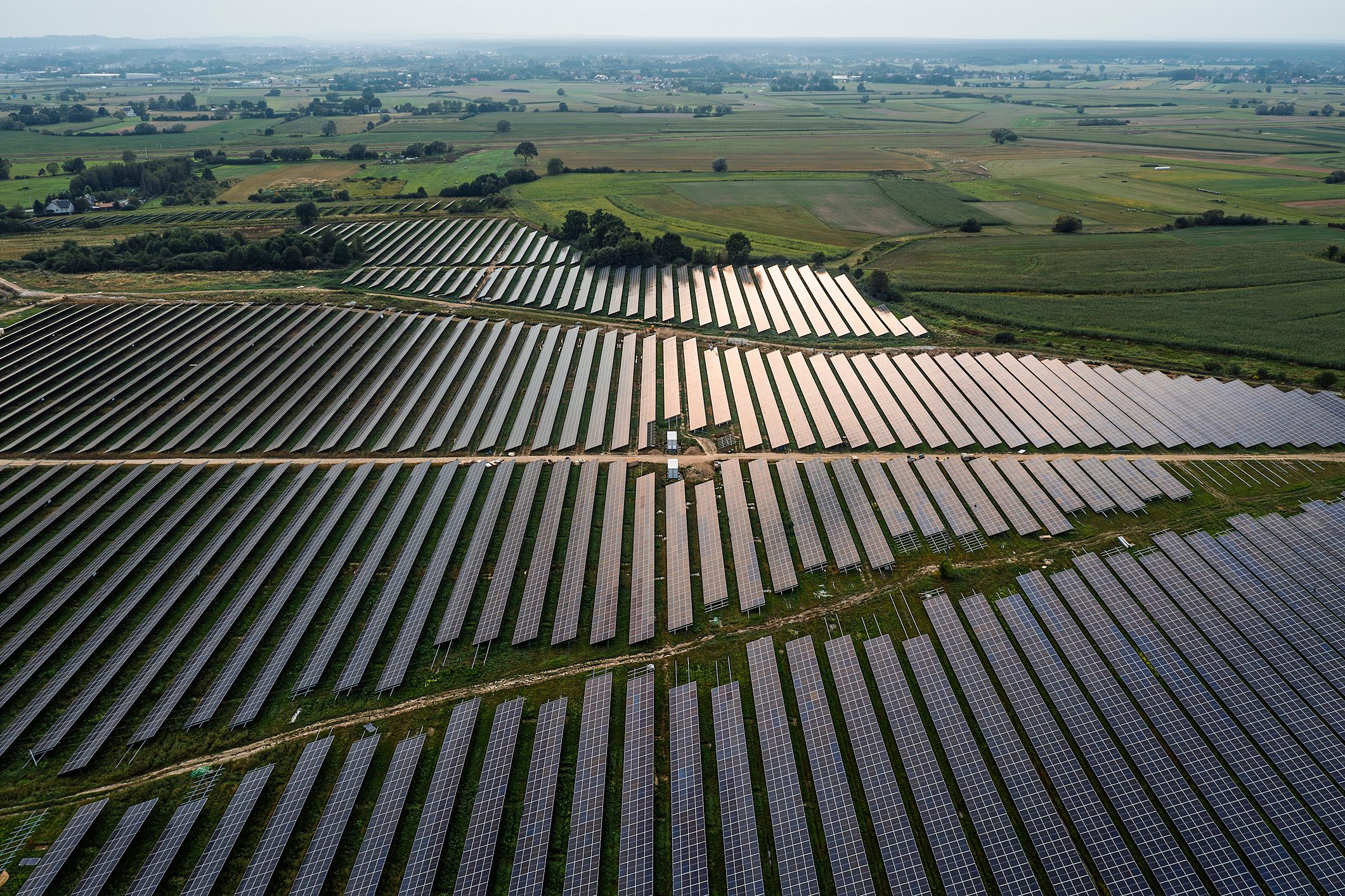 Aerial view of a large photovoltaic power plant under construction, among green fields.